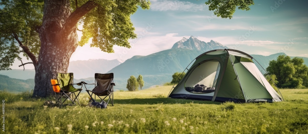 Poster campsite with white tent tree green grass mountain backdrop camping gear chairs copy space image pla