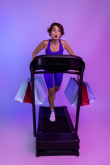 Photo of surprised sportive girl running treadmill with packages buy on sport store sale isolated ultraviolet color background