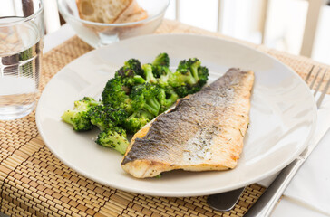 Fried fillet of sea bass with garnish of broccoli on black warm stone plate