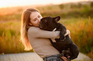 Woman holds in her arms, kisses a dog, looks at him lovingly,at sunset.The concept of...