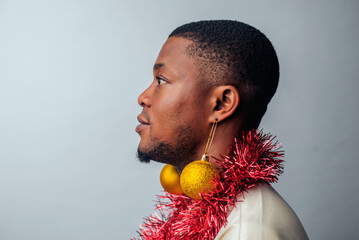 A profile view of a man styled in Xmas  balls as earrings and sash