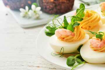 Stuffed or deviled eggs yolk, shrimp, pea microgreens with paprika for easter table decorate fresh cherry or apple blossoms on white light background. Happy Easter traditional dish concept. Mock up.