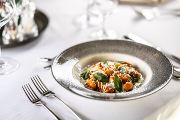 Gnocchi pomodoro with mascarpone, cream, basil and parmesan, in a stylish plate on a restaurant table
