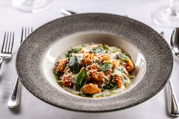 Gnocchi pomodoro with mascarpone, cream, basil and parmesan, in a stylish plate on a restaurant table