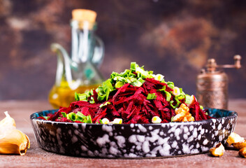 Beetroot salad with wallnuts and garlic in bowl on wooden table. Selective focus.