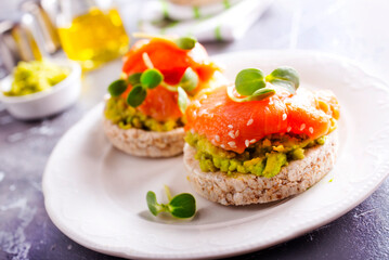open sandwiches with rye bread, avocado, smoked salmon on a white plate