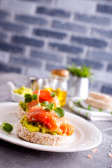open sandwiches with rye bread, avocado, smoked salmon on a white plate