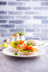 open sandwiches with rye bread, avocado, smoked salmon on a white plate