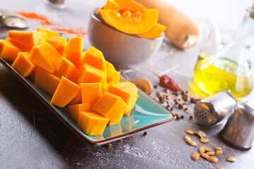 Diced pumpkin pieces in a bowl, with spices and olive oil at home