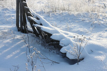 The remaining part of a fallen wooden fence covered with snow