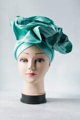 teal turban on a mannequin head, pleated teal fashion turban on a white background
