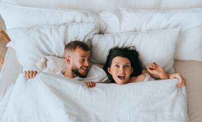 Excited couple laying in bed amazed by great news about pregnancy. Newlyweds in bed on honeymoon....