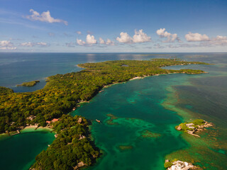 Aerial drone view from above of the tropical Caribbean island with lush green palm trees forests and sandy beaches surrounded with crystal clear turquoise ocean water.