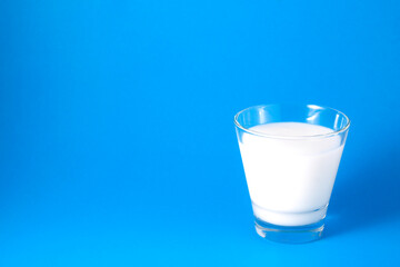 Milk in a clear glass on a blue background.