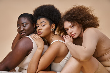 expressive body positive women in underwear posing and looking at camera on beige, self-confidence