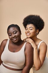 cheerful african american female models in underwear looking at camera on beige, plus size beauty