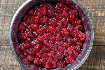 Fresh red raspberry berry, covered with granulated sugar for jam preparation in bowl, top view, closeup. Background and texture of raspberries with sugar