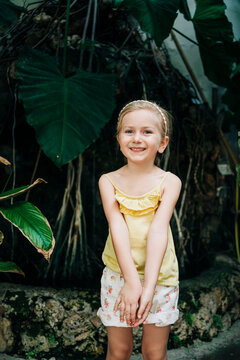 A young girl with pigtails looks curiously at a diverse collection of cacti in terracotta pots in a sunny greenhouse