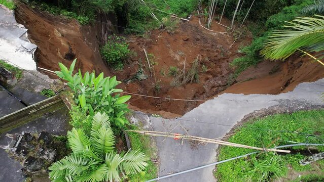 Camera fly up and show landslide area from above, village road destroyed, ground from steep slope of ravine collapsed down. House fence hang over cliff, destabilized soil is prone to further collapse