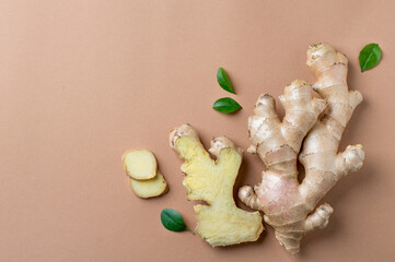 Fototapeta premium Composition of whole and chopped ginger root, green leaves on a light, beige background. Horizontal, free copy space.
