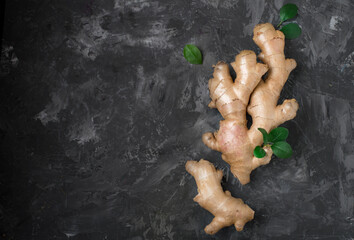 Raw ginger root and green leaves on a dark background. Horizontal, free space for printing..