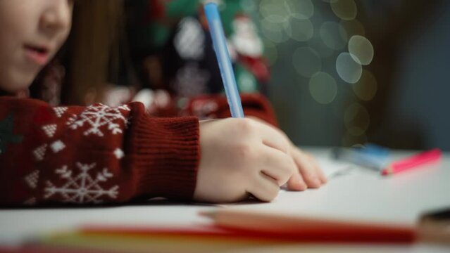 A close-up of a child's hand writing with a pen on a piece of Santa's letter. Celebrating Christmas, gifts for the holiday, fairy tale atmosphere. High quality 4k footage