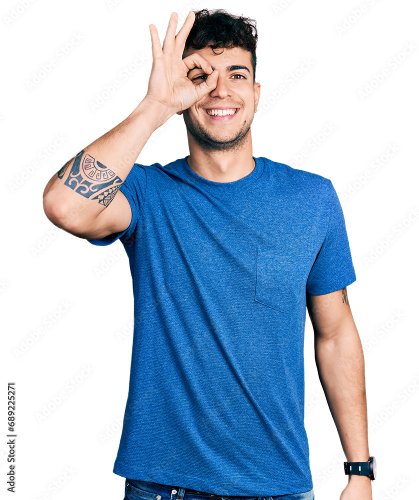 Canvas Prints Young hispanic man wearing casual t shirt doing ok gesture with hand smiling, eye looking through fingers with happy face.