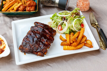 BBQ Grilled pork ribs and potato fries with barbecue sauce and ketchup and grilled vegetables