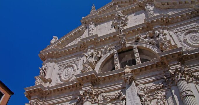 Imposing facade of San Mois&egrave; church with classical sculptures and ornate details against a clear blue sky in Venice, Italy, framed by vibrant buildings.