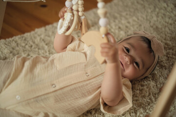 Engrossed in play, a baby reaches for wooden rings, supported by a loving hand. Symbolizes the...