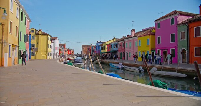 Glimpse into the vibrant life of Burano, Venice with a canal view framed by colorful houses and moored boats, reflecting the island's unique charm.
