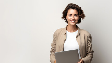 Woman with brown hair, wearing a beige jacket holding a laptop, against grey background.