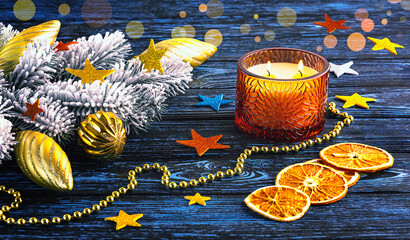 Christmas and New Year composition with a burning candle, snowy Christmas tree branch and Christmas decorations on a dark blue background.