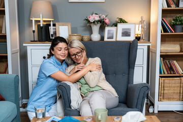 Young woman doctor health care worker medic nurse comforting older senior woman at home visit,...