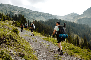 Group of people with backpacks and nordic walking sticks on a hiking path in Switzerland Alps during summer time
