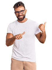 Young hispanic man wearing casual clothes and glasses pointing to the back behind with hand and...