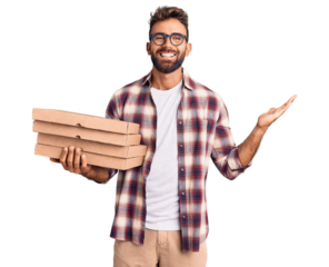 Young hispanic man holding delivery pizza box celebrating victory with happy smile and winner expression with raised hands