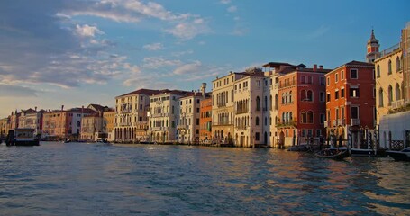 Sunset view of the Grand Canal in Venice, with historical buildings lining the waterway and gondolas docked along the banks. Dusk light casting a warm glow on facades.