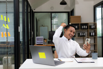 A businessman wearing a formal suit is at work. He sat in front of his laptop computer, raised his hand and shouted with great joy. About success in business and celebrations