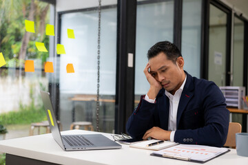 Tired Millennial businessman sitting at laptop touching head feeling tired overworked Suffering...