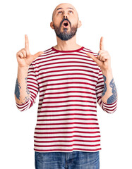 Naklejka premium Young handsome man wearing casual clothes amazed and surprised looking up and pointing with fingers and raised arms.