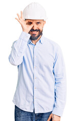 Young handsome man wearing architect hardhat doing ok gesture with hand smiling, eye looking through fingers with happy face.