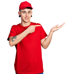 Young caucasian boy with ears dilation wearing delivery uniform and cap amazed and smiling to the camera while presenting with hand and pointing with finger.