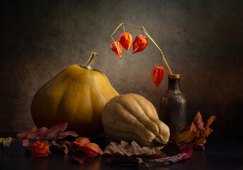 Still life with two pumpkins and dry autumn leaves on a dark background