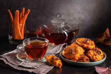 Carrot cookies with walnuts and tea in a cup against a dark background