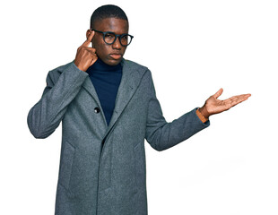 Young african american man wearing business clothes and glasses confused and annoyed with open palm showing copy space and pointing finger to forehead. think about it.
