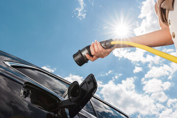 Woman plugging in the charger into electric car at a charging station in the street