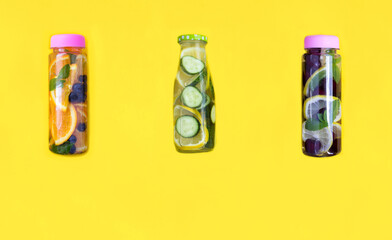 Infused or detox water with fruit, berry and vegetable n the bottles on the yellow background. Copy space.