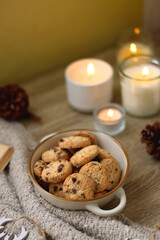 Bowl of cookies, cup of tea, dry oranges, pine cones, books, reading glasses, small presents, various Christmas decorations and lit candles on the table. Cozy Christmas hygge. Selective focus.