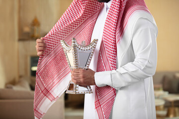 An Arab man holds a censer and perfumes himself with its smoke